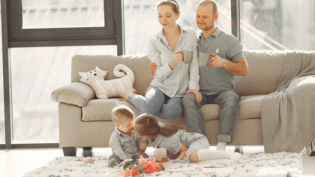 Cheerful family smiling while spending weekend together sitting parents sitting on comfortable sofa while children resting on carpet and playing